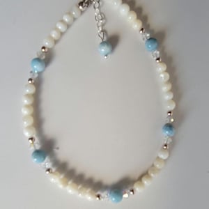May include: A white and blue beaded anklet with a silver clasp. The anklet features white shell beads, light blue gemstone beads, and clear crystal beads.