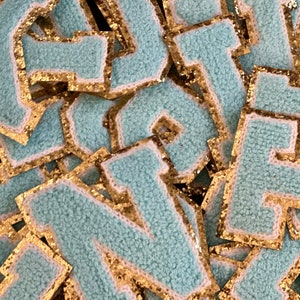 May include: A pile of light blue felt letters with gold glitter trim. The letters are in a variety of styles and sizes.