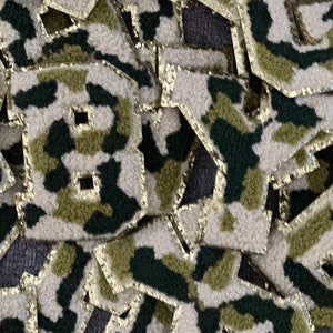 May include: A pile of felt patches in a camouflage pattern with gold glitter trim. The patches are shaped like the letter "B".