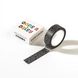 May include: A white box with the words "oops a daisy" in colourful letters and social media icons. A roll of black washi tape with white text unspools next to the box. The tape has quotes printed on it.