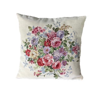 Könnte beinhalten: Ein weißes Kissen mit einem Blumendesign mit rosa, roten, violetten und gelben Blumen. Die Blumen sind in einem Strauß angeordnet und von grünen Blättern umgeben.