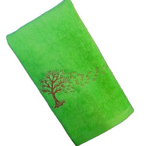 Könnte beinhalten: Ein grünes Handtuch mit einem roten gestickten Baum und Blättern, die im Wind wehen.