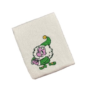 Könnte beinhalten: Weißes Armband mit einem gestickten grünen Elf, der einen rosa Hut trägt und ein grünes Geschenk hält. Der Elf hat einen gelben Stern auf seinem Hut.