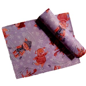 Könnte beinhalten: Lilafarbene Stoff-Platzsets mit einem sich wiederholenden Muster aus rosa Schweinen, die auf einem schneebedeckten Hintergrund Schlittschuh laufen. Die Platzsets haben ein weißes Schneeflockenmuster.
