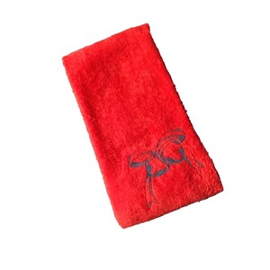 Könnte beinhalten: Rotes Frottierhandtuch mit einem blauen gestickten Bogen.