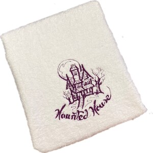 Könnte beinhalten: Weißes Küchentuch mit einem lila gestickten Design eines Spukhauses mit Vollmond und dem Text "Haunted House".