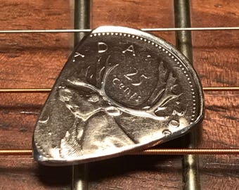 Könnte beinhalten: Eine silberne kanadische 25-Cent-Münze mit einem Elch wurde zu einem Gitarrenplektrum umgewandelt.