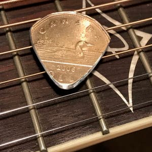 Puede incluir: Una moneda canadiense de un dólar de 2006, con un colimbo, se ha reutilizado como púa de guitarra.