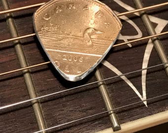 Könnte beinhalten: Eine kanadische Ein-Dollar-Münze aus dem Jahr 2006 mit einem Seetaucher wurde zu einem Gitarrenplektrum umfunktioniert.