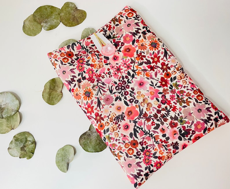 May include: A white fabric pouch with a floral print in shades of pink, red, and brown. The pouch has a small white tag with a pink button.