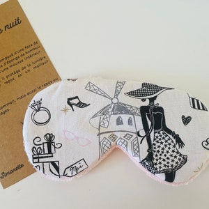 May include: A sleep mask with a Parisian theme, featuring a black and white illustration of a woman in a hat, a windmill, and other Parisian icons. The mask has a pink interior and a gold elastic band.