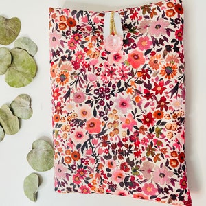May include: A small, floral patterned pouch with a pink button closure. The pouch is made of a soft, cream-colored fabric with a variety of pink, red, and orange flowers.