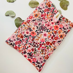 May include: A white fabric pouch with a floral pattern in shades of pink, red, and brown. The pouch has a small white button on the front.