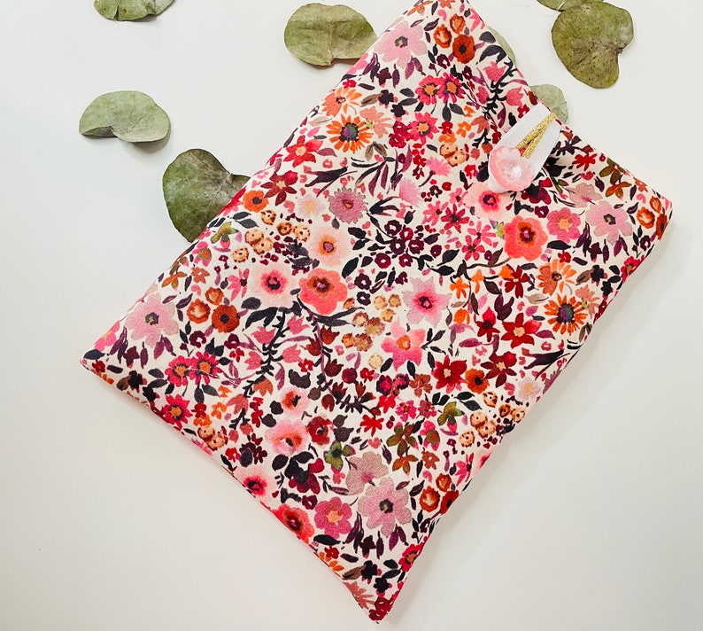 May include: A white fabric pouch with a floral pattern in shades of pink, red, and brown. The pouch has a small white button on the front.