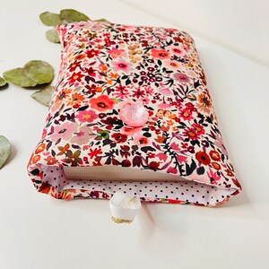 May include: A book cover with a floral pattern in shades of pink, red, and white. The cover has a white button and a white ribbon bookmark.