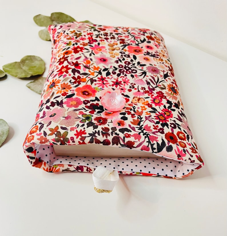 May include: A book cover with a floral pattern in shades of pink, red, and white. The cover has a white button and a white ribbon bookmark.