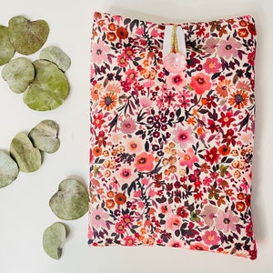 May include: A small, white fabric pouch with a floral pattern in shades of pink, red, and orange. The pouch has a white ribbon and a pink button closure.