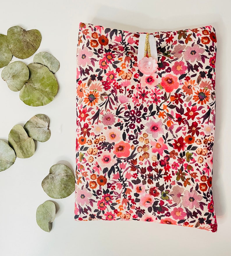 May include: A small, white fabric pouch with a floral pattern in shades of pink, red, and orange. The pouch has a white ribbon and a pink button closure.