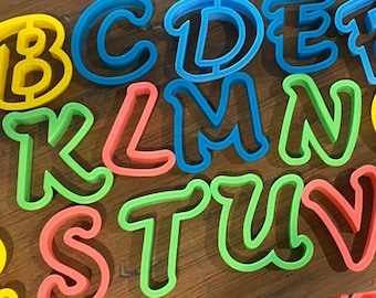 May include: A set of colorful plastic alphabet cookie cutters. The cutters are arranged in alphabetical order, with the letters A through Z.