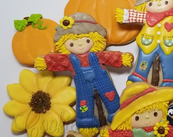 May include: A set of 10 decorated sugar cookies featuring fall themes. The cookies are decorated with various fall colors, including orange, yellow, green, and brown. The cookies depict pumpkins, sunflowers, and scarecrows. The text "Cookies by Cindy Bryan" is visible in the top right corner of the image.