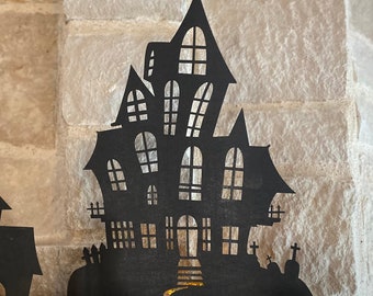 May include: Black silhouette of a haunted house with a winding path leading to the front door. The house has multiple windows and a pointed roof.