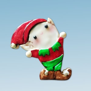 May include: A red and green Christmas elf ornament with a white face and brown boots. The elf is smiling and has a pointy hat.