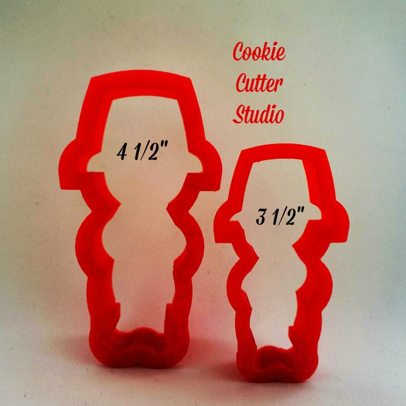 May include: Two red plastic cookie cutters shaped like people. The larger cutter is 4 1/2 inches tall and the smaller cutter is 3 1/2 inches tall. Cookie Cutter Studio.