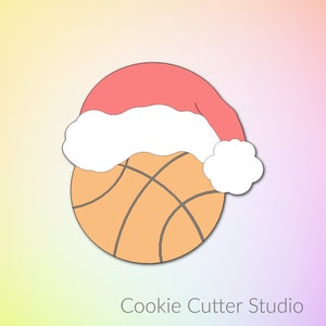 May include: A cookie cutter shaped like a basketball wearing a Santa hat. The basketball is orange with black lines and the hat is red with white trim.