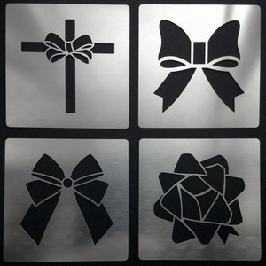 May include: Four metal stencils featuring different bow designs. The stencils are silver and have a brushed metal finish. The designs include a simple bow, a bow with a cross, a bow with a knot, and a bow with a star.