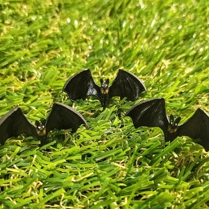 May include: Three black plastic bats with a slightly shiny finish are arranged in a triangular pattern on a green artificial grass surface.