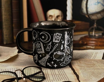 Puede incluir: Taza de cerámica negra con un diseño blanco de un caldero, una escoba, una luna creciente y la palabra "Spells".