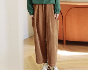 May include: Brown corduroy pants with a wide leg and pleats. The pants have large pockets on the sides and a relaxed fit.