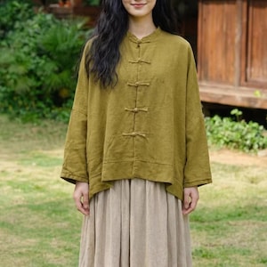 May include: Olive green long-sleeved top with a mandarin collar and frog closures. The top has a relaxed fit and is paired with a beige skirt. The outfit is made of a soft, flowing fabric, suitable for casual wear.