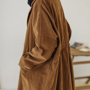 May include: A long brown corduroy coat with a collar and long sleeves. The coat has a drawstring waist and pockets.