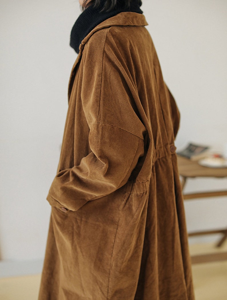 May include: A long brown corduroy coat with a collar and long sleeves. The coat has a drawstring waist and pockets.