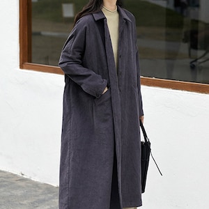 May include: A long, dark gray, collared, button-up coat with pockets. The coat is made of a soft, textured fabric.