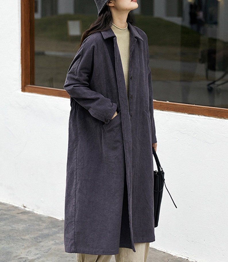 May include: A long, dark gray, collared, button-up coat with pockets. The coat is made of a soft, textured fabric.