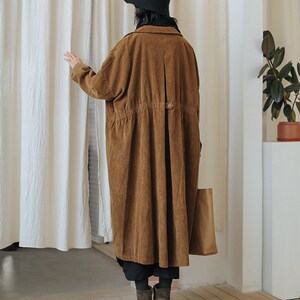 May include: A long brown corduroy coat with a button closure and a drawstring waist. The coat has a relaxed fit and is perfect for layering.