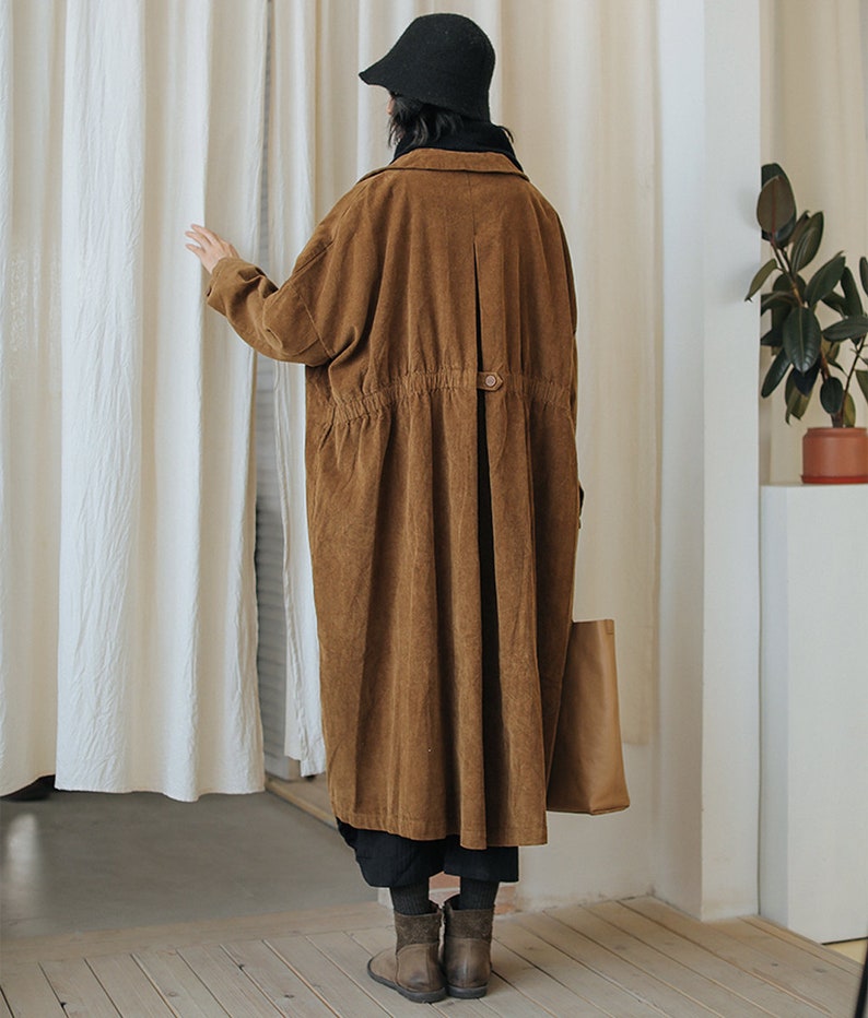 May include: A long brown corduroy coat with a button closure and a drawstring waist. The coat has a relaxed fit and is perfect for layering.