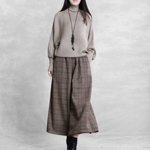 May include: A beige turtleneck sweater with a black beaded necklace and brown plaid wide-leg pants.