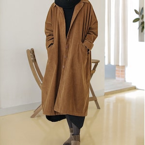 May include: A long brown corduroy coat with a button-up front and pockets. The coat has a relaxed fit and is made of a soft, comfortable fabric.