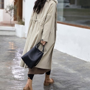 May include: A beige long-sleeved coat with a drawstring waist and a black tote bag.