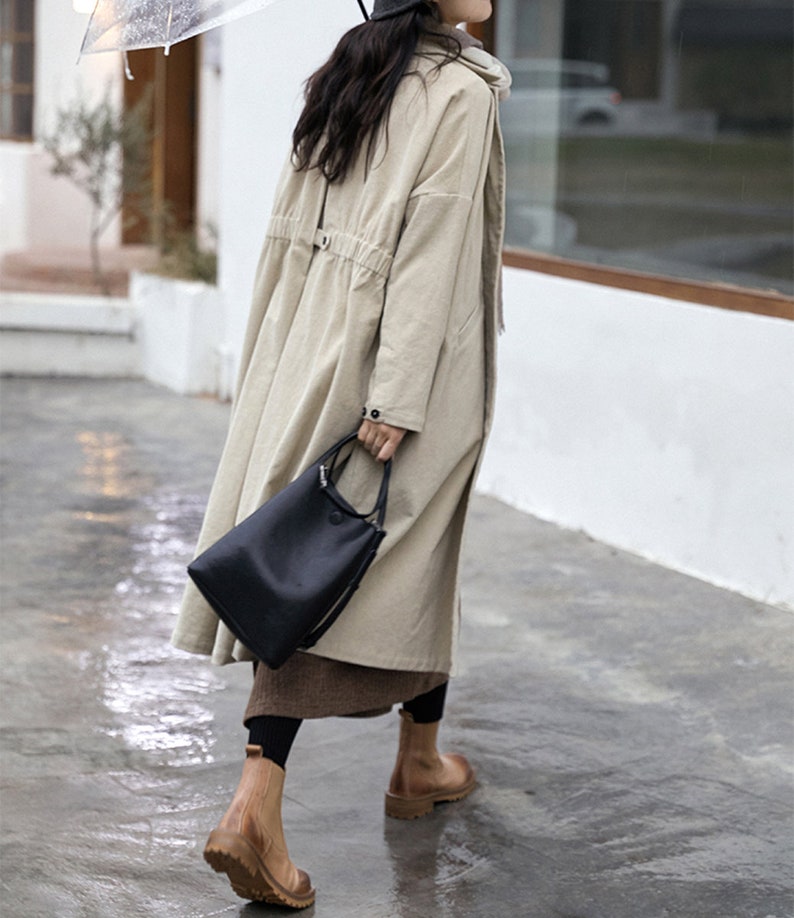 May include: A beige long-sleeved coat with a drawstring waist and a black tote bag.