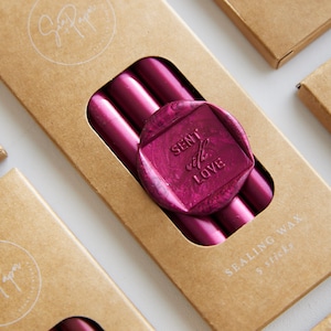 May include: A set of five sealing wax sticks in a deep pink colour, packaged in a brown box with the text "Sent with Love" on a pink wax seal. The box also says "Sealing Wax 5 Sticks".