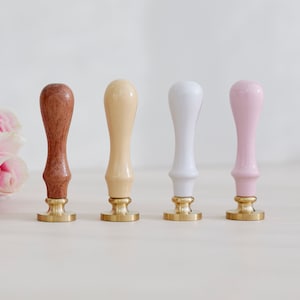 May include: Four wooden wax seal stamps with gold bases. The stamps are in different colours: brown, beige, white, and pink.