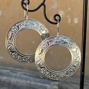 Peut inclure: Une paire de boucles d'oreilles créoles en argent avec un motif complexe d'animaux et de fleurs autour du bord.