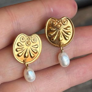 Può includere: Orecchini d'oro con un ciondolo di perla. Gli orecchini presentano un design circolare con dettagli intricati.