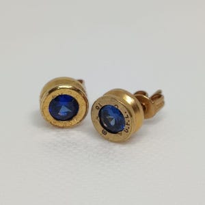 Peut inclure: Une paire de boucles d'oreilles en or avec une pierre de saphir bleu au centre. Les boucles d'oreilles ont un design circulaire avec les mots "925 Italy" gravés au dos.