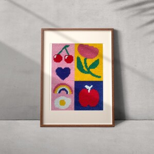 Peut inclure: Une &oelig;uvre d'art encadr&eacute;e avec un motif cousu en quatre carr&eacute;s. Les carr&eacute;s contiennent des images de cerises, d'un c&oelig;ur, d'un arc-en-ciel et d'une pomme. Les couleurs de fond sont rose, jaune et bleu. Le cadre est de couleur marron chaud.