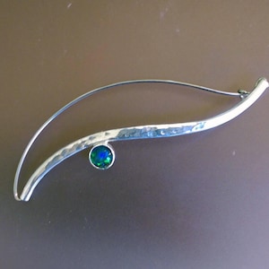 May include: A silver brooch with a hammered finish and a green opal gemstone.
